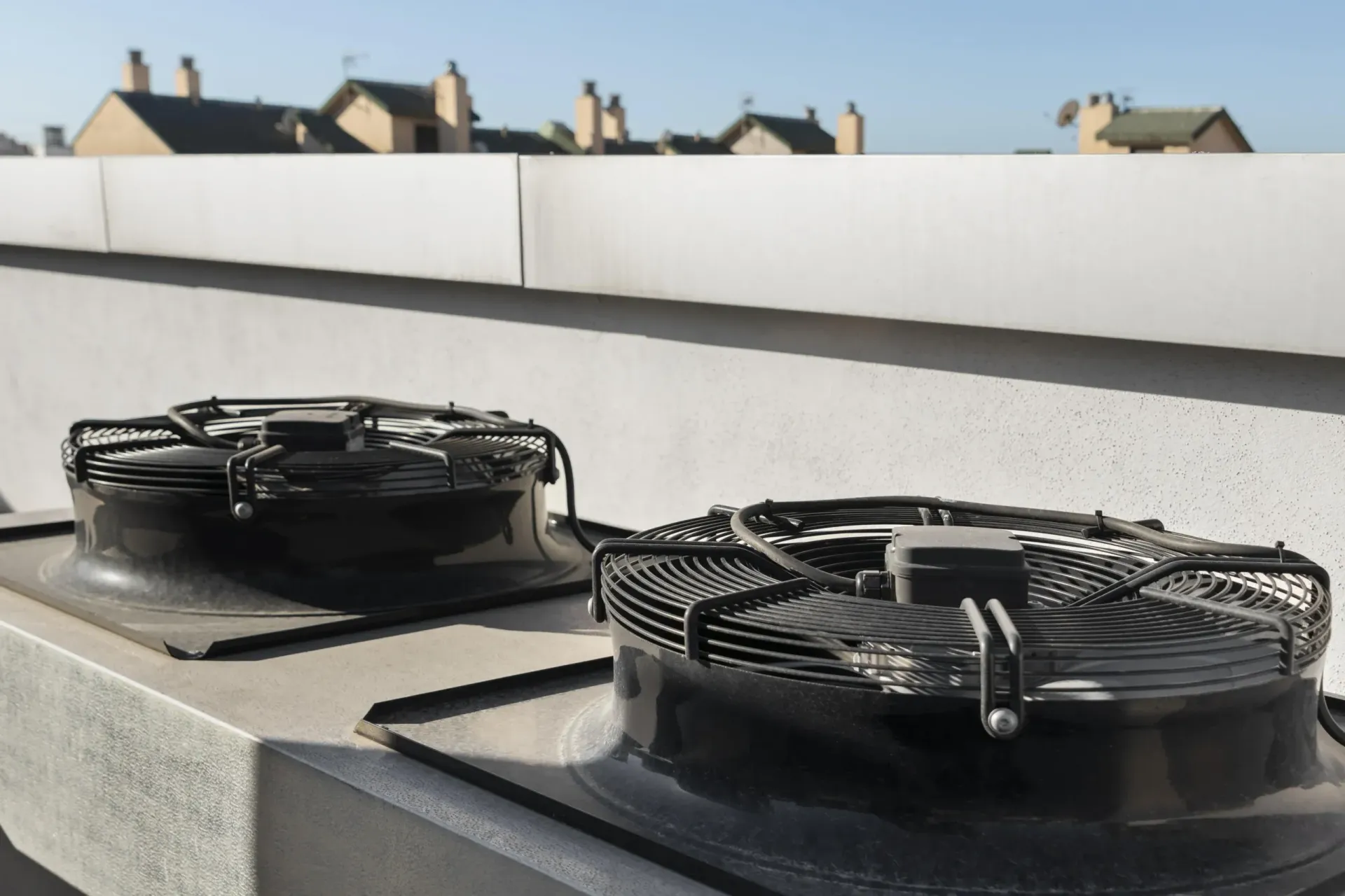 Two rooftop ventilation fans on a flat roof with houses visible in the background