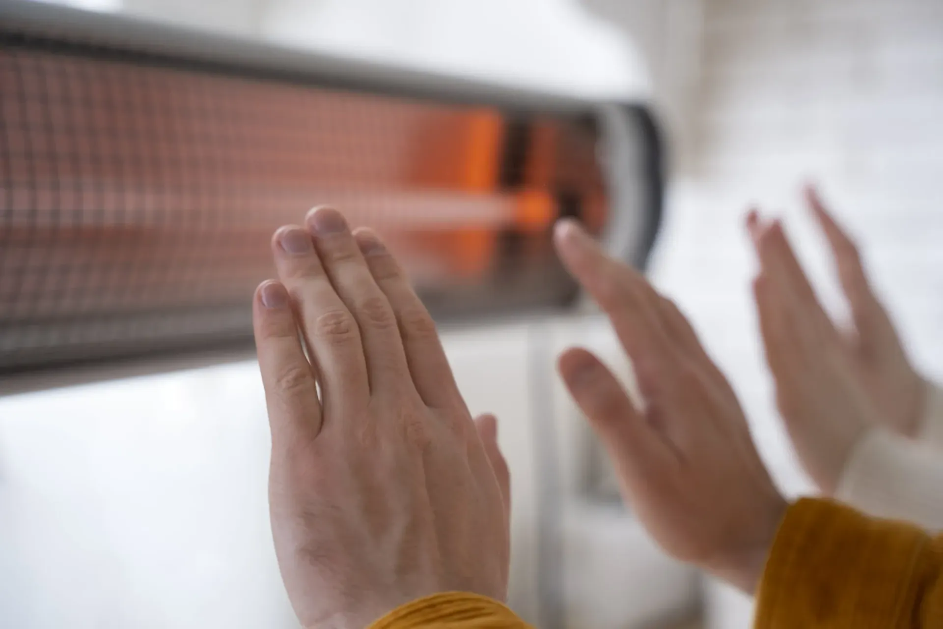 Hands warming near a wall-mounted electric heater with glowing orange coils