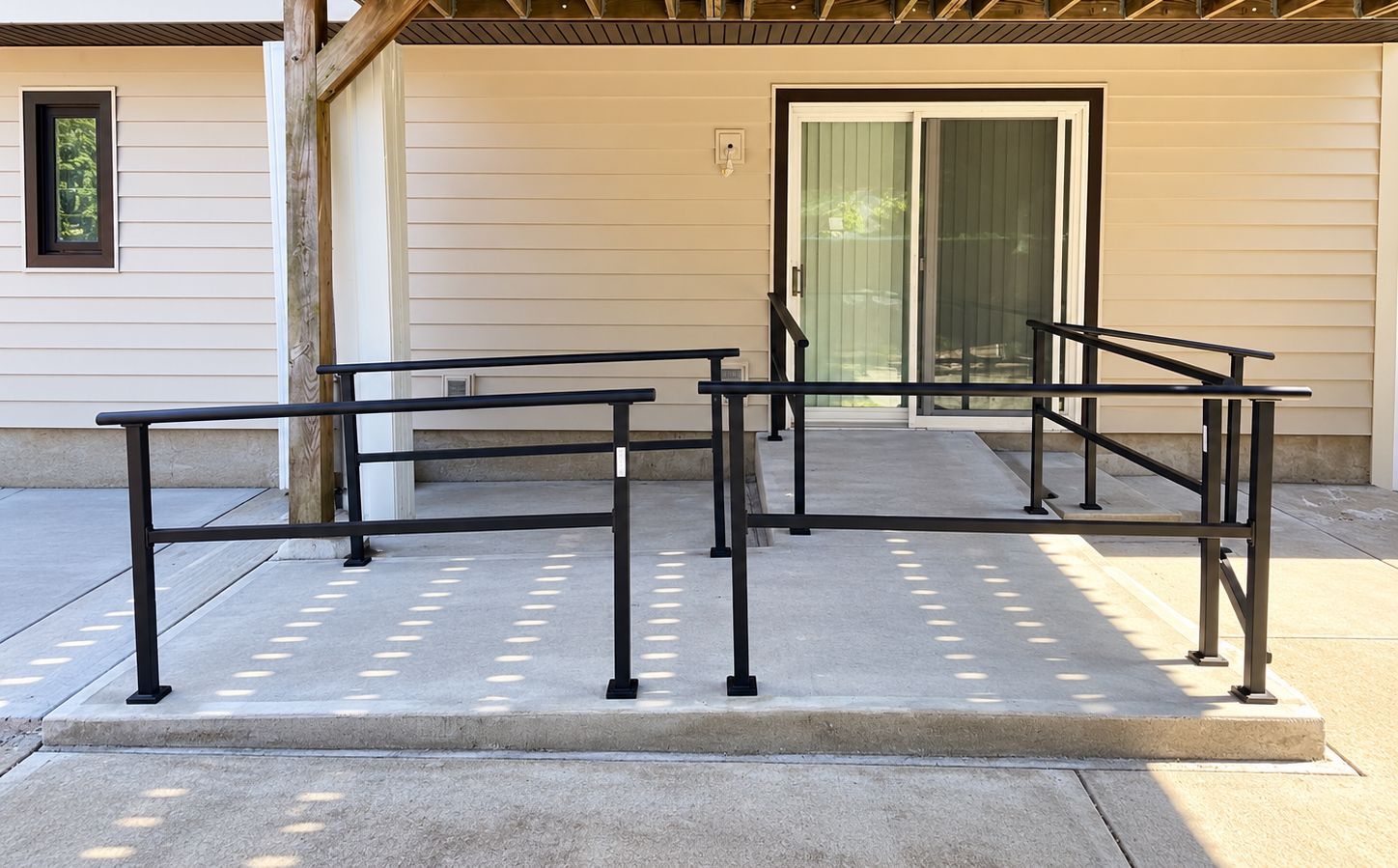 Accessible ramp and handrails leading to a sliding glass door on a beige building exterior.