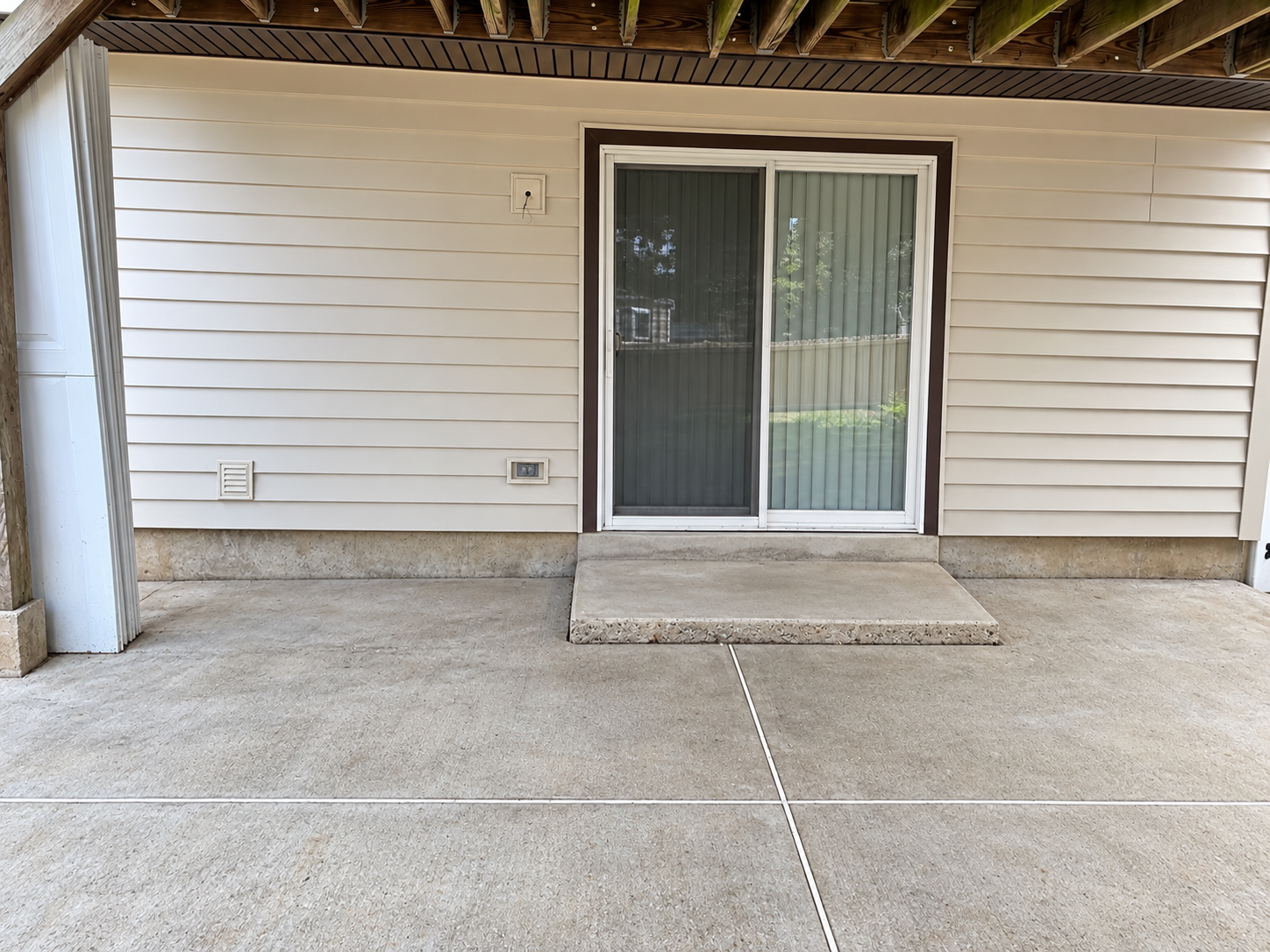 Covered patio with concrete floor, sliding glass door, and white siding on a house.