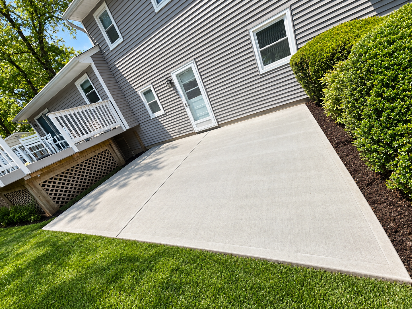 Freshly poured concrete driveway beside a gray house with white trim and green hedges