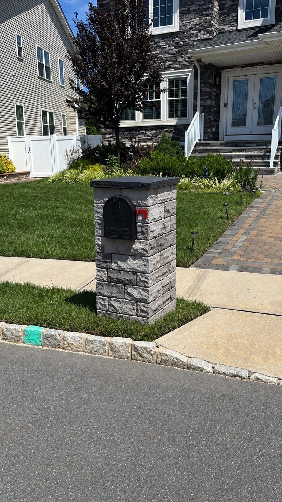Stone mailbox post by a suburban sidewalk in front of a house and lawn