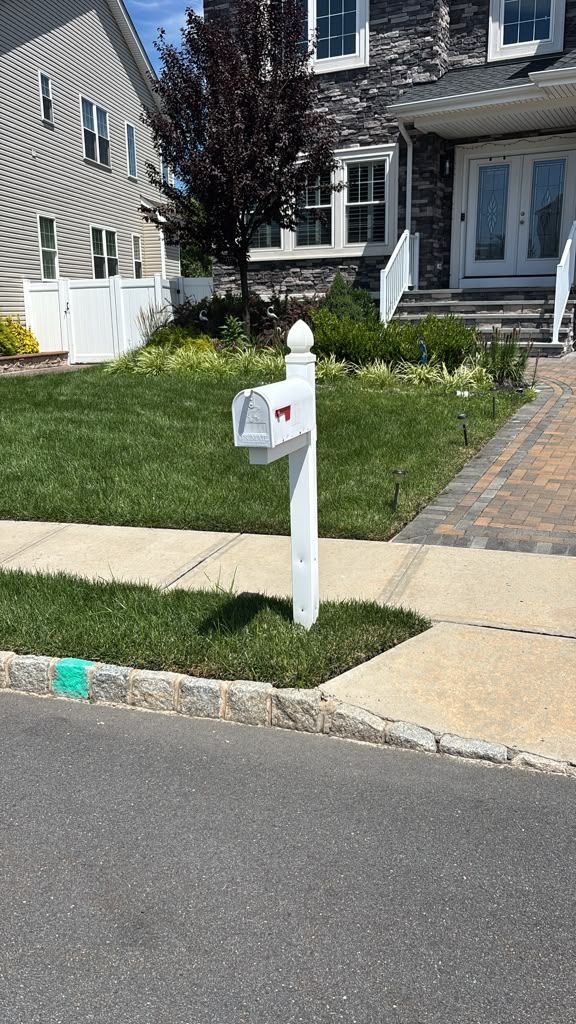 White mailbox on a post beside a sidewalk in front of a suburban house and lawn