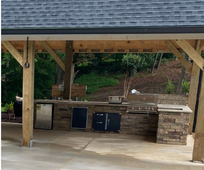An outdoor kitchen under a wooden structure with a roof