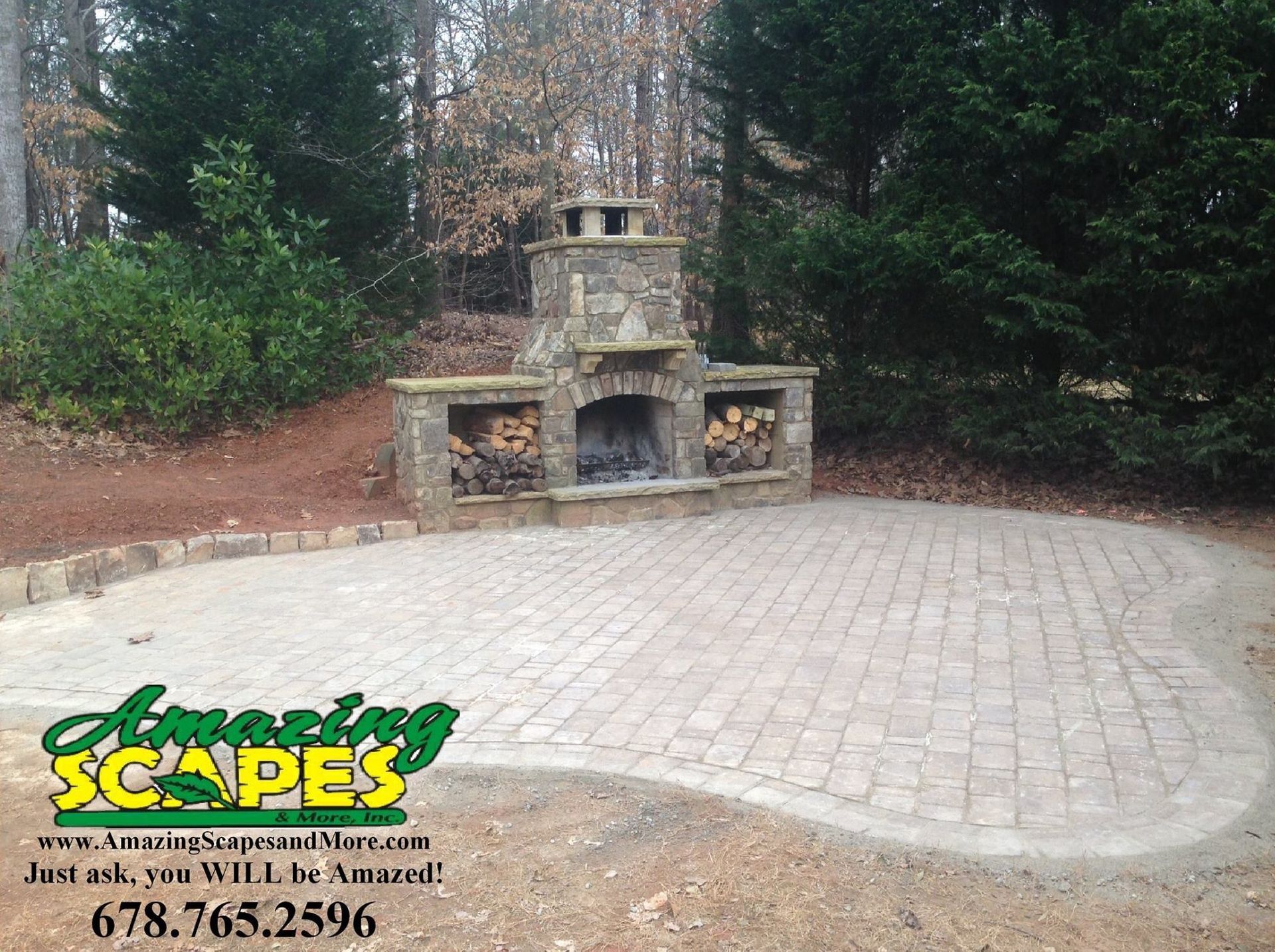 A stone fireplace sits on a brick patio surrounded by trees