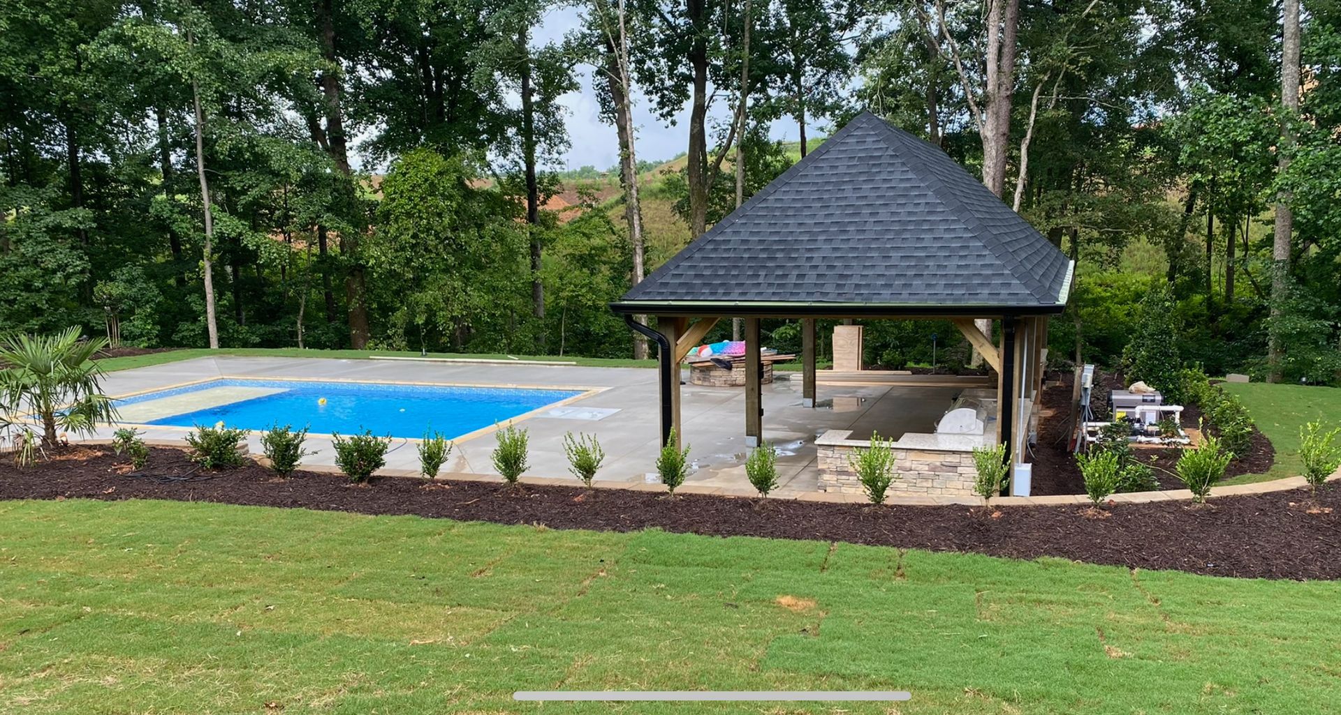 A large swimming pool with a gazebo in the backyard surrounded by trees.