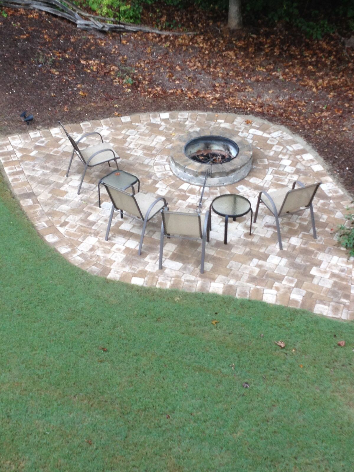 A fire pit is surrounded by chairs and tables on a patio.