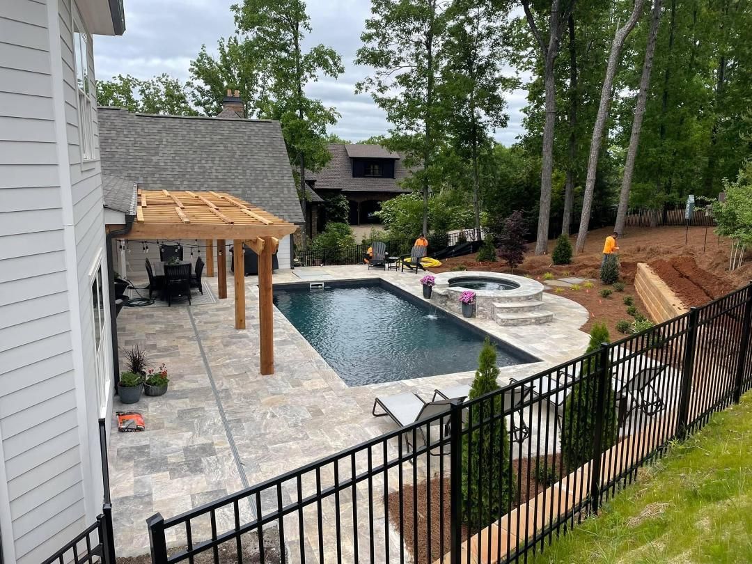 A large swimming pool is surrounded by a fence and a pergola.