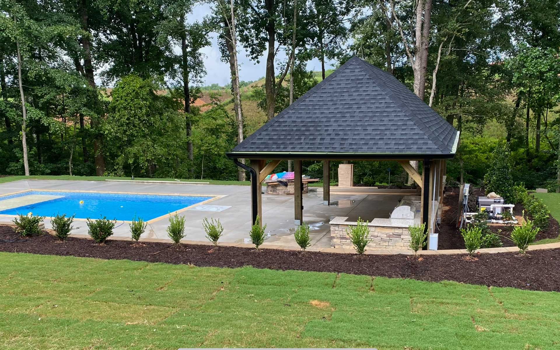 A gazebo is sitting in the middle of a lush green field next to a swimming pool.