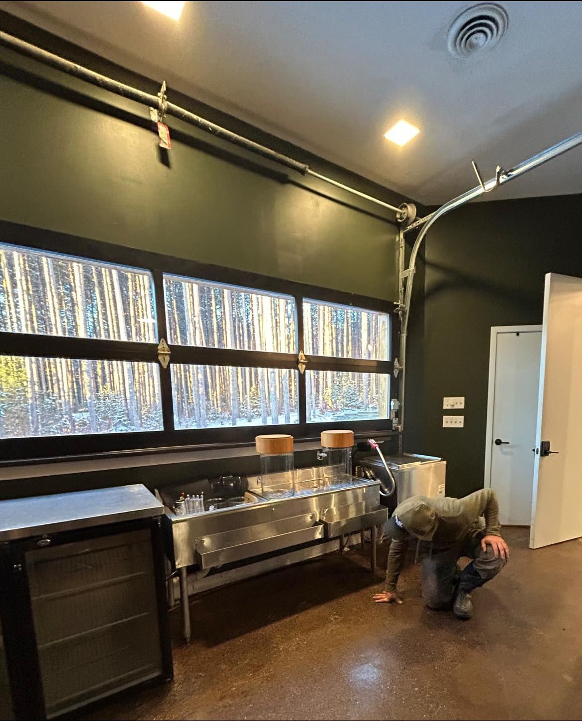 A man is kneeling in front of a stainless steel sink in a kitchen.