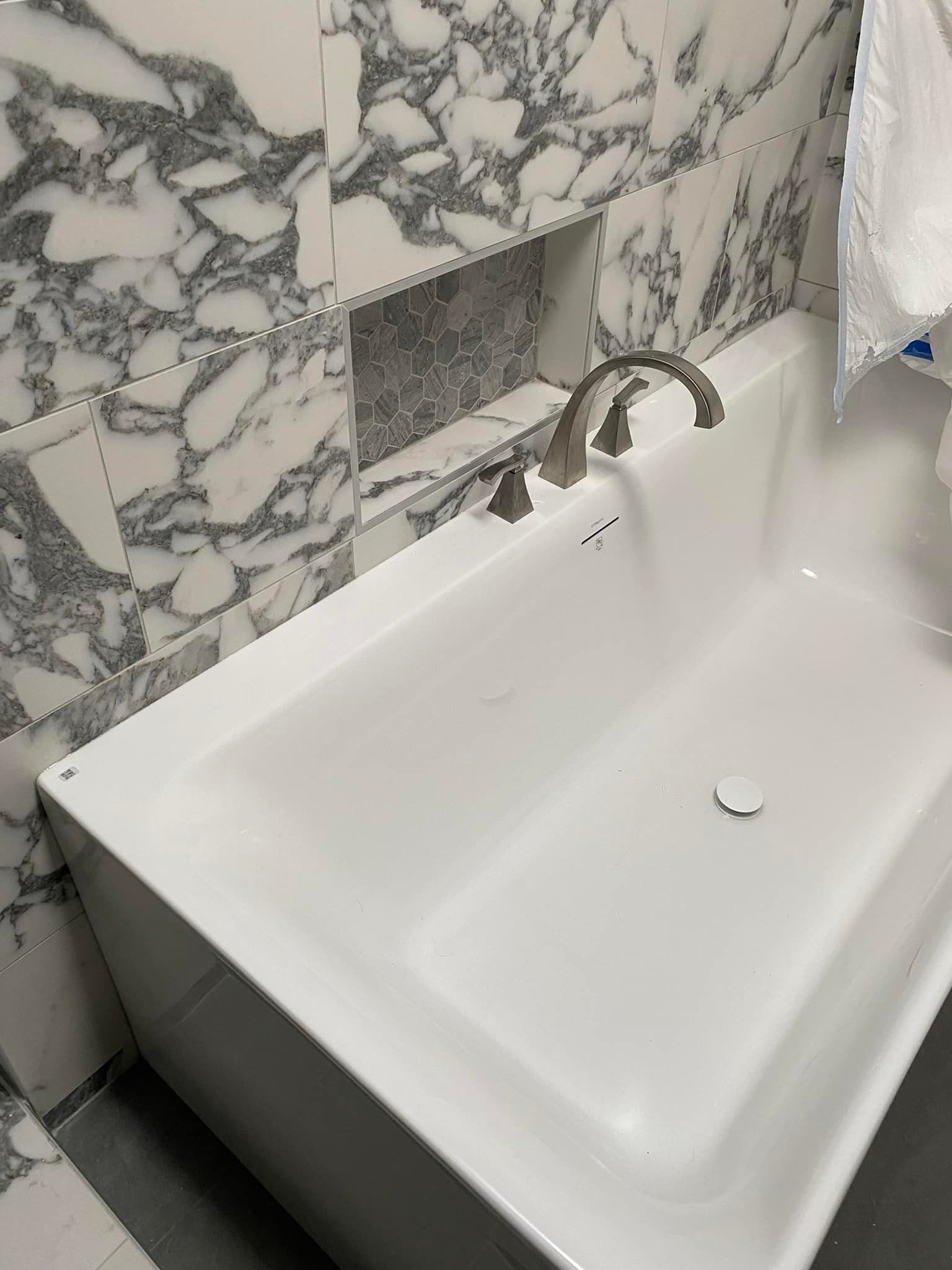 A white bathtub is sitting in a bathroom next to a marble wall.