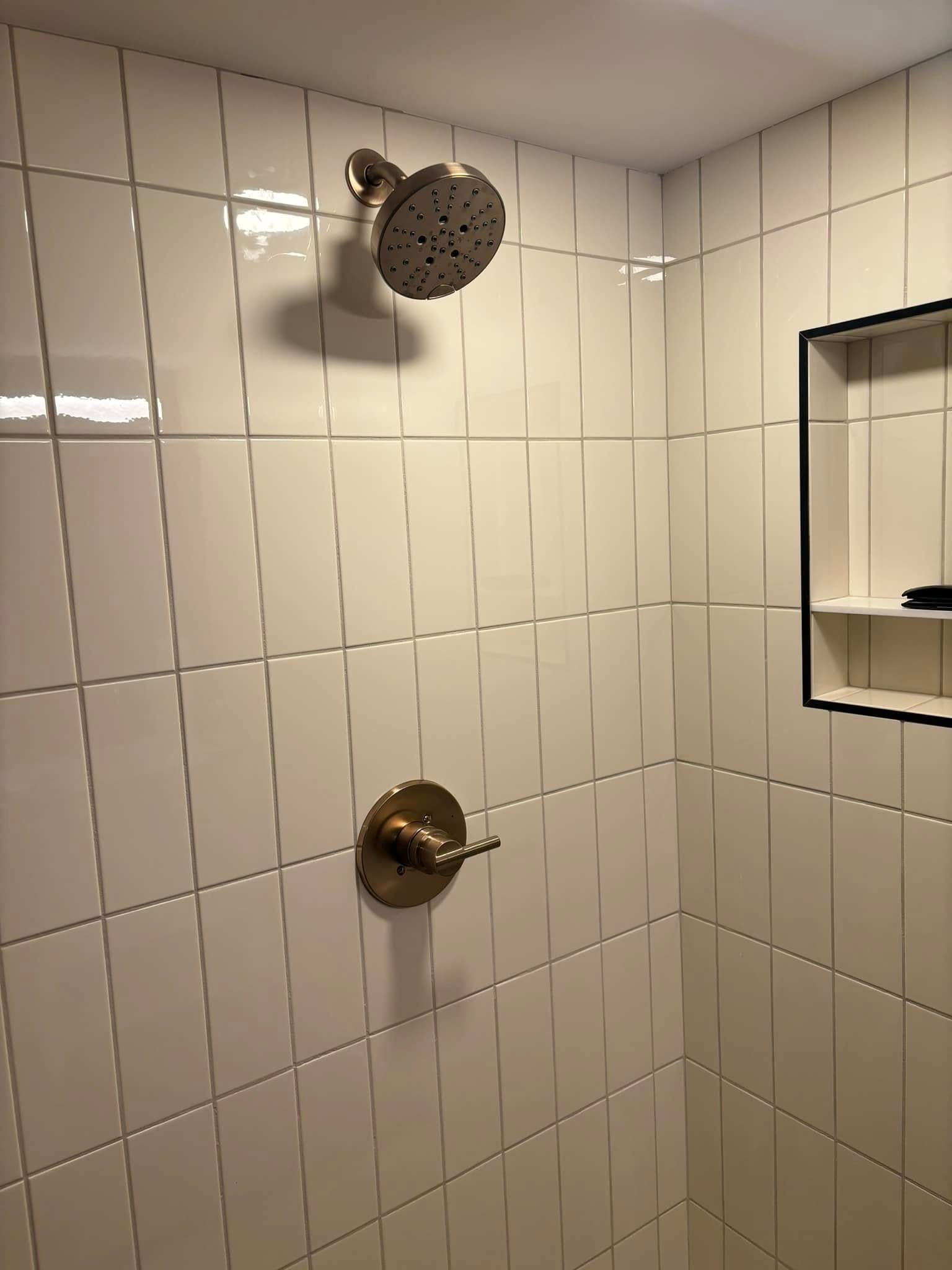 A shower head is hanging from the ceiling in a bathroom with white tiles.
