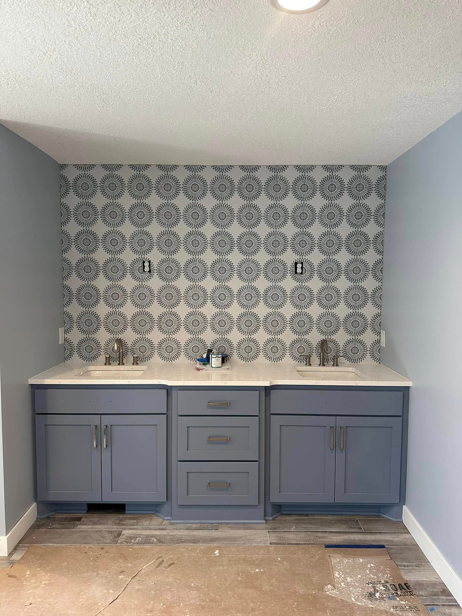 A bathroom with a sink , cabinets , and wallpaper on the wall.