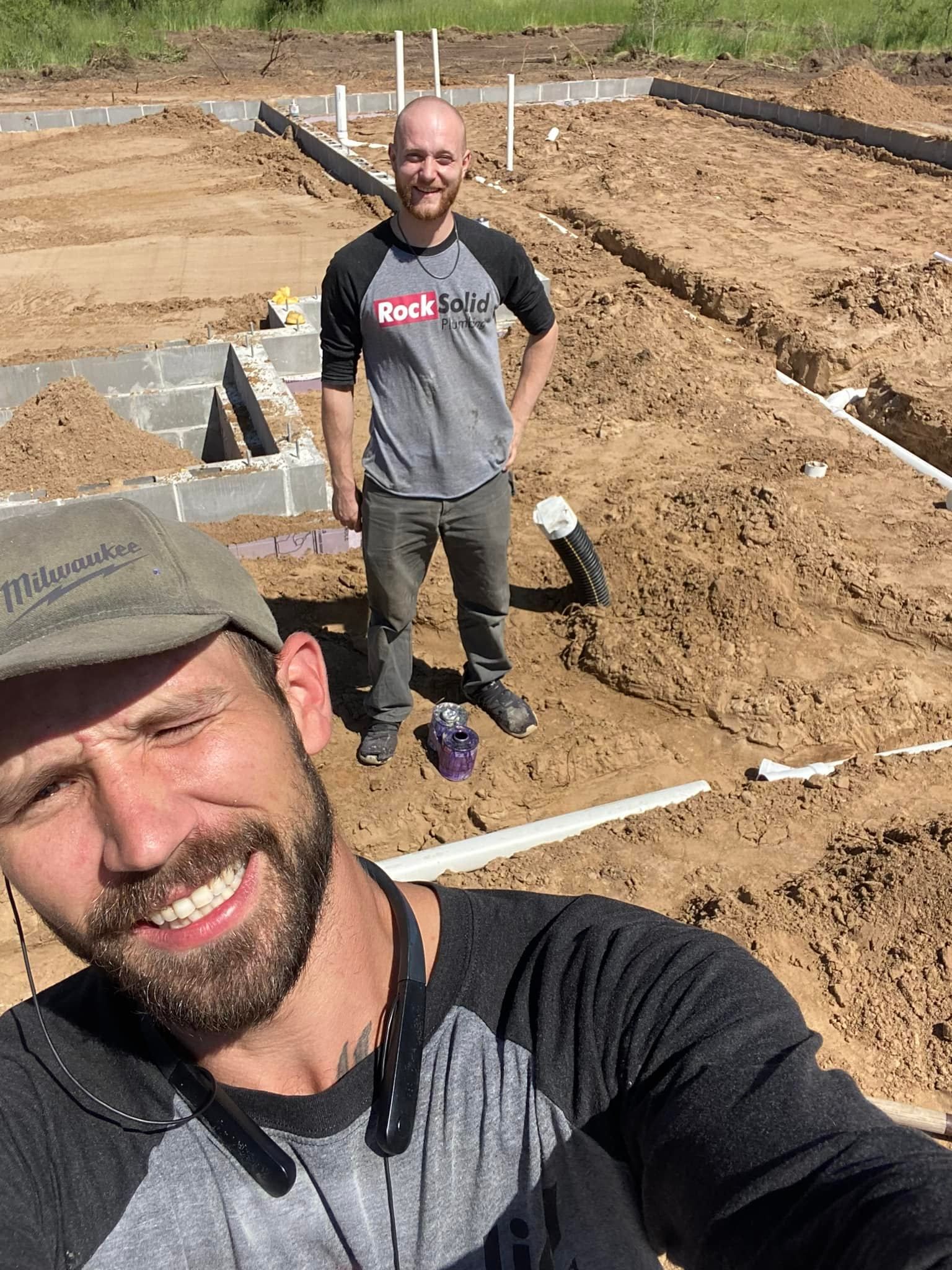 Two men are standing next to each other in the dirt on a construction site.