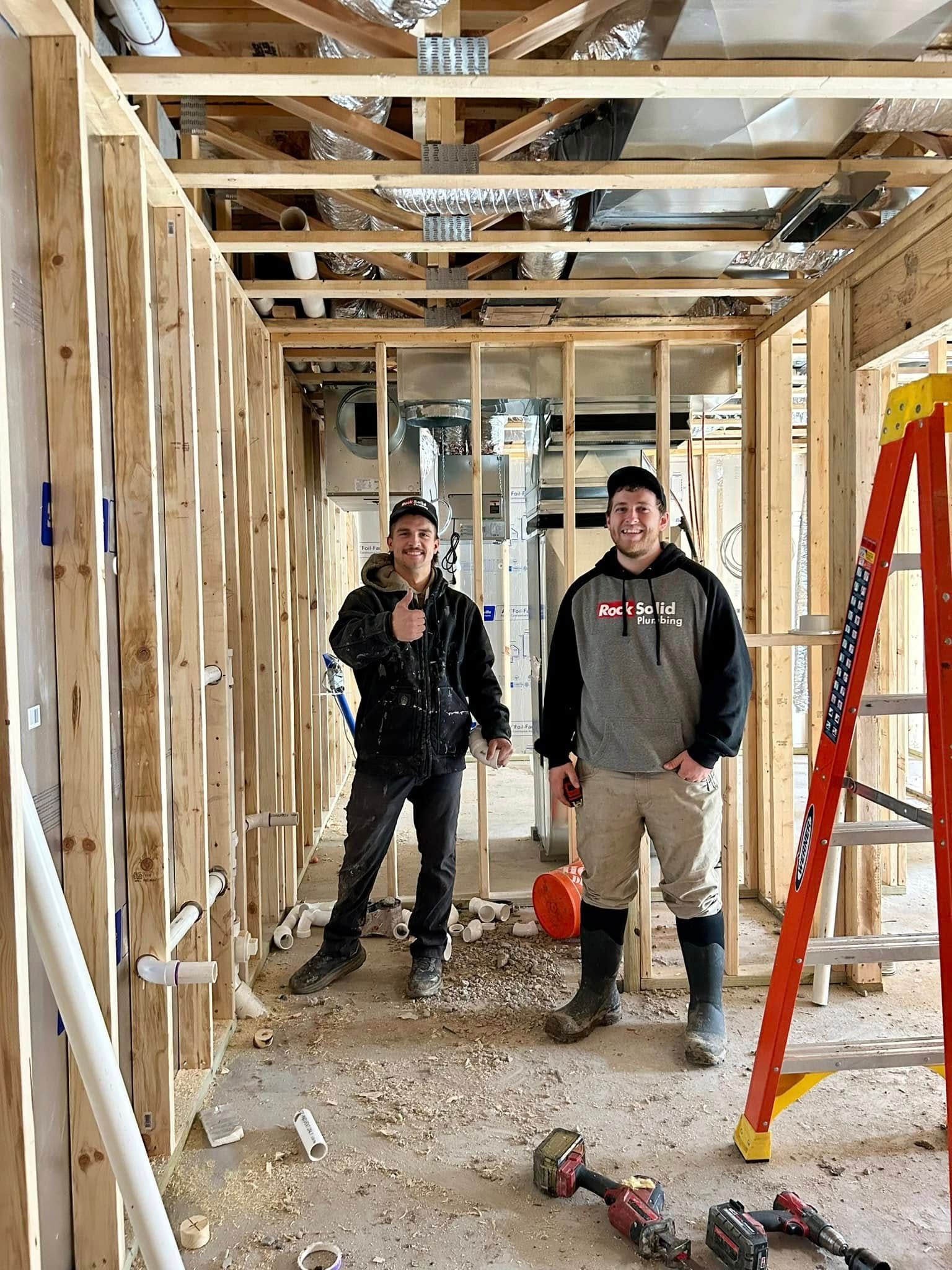 Two men are standing in a room under construction next to a ladder.