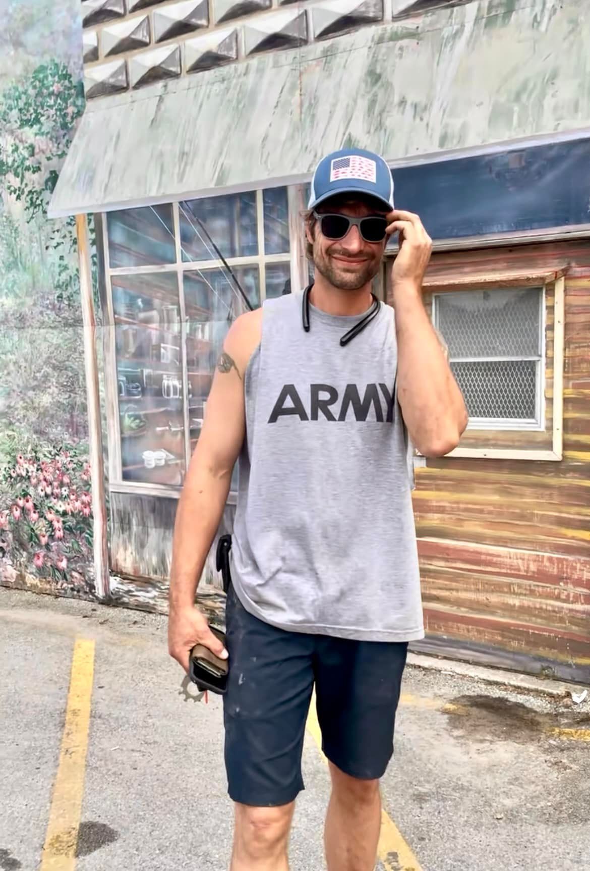 A man wearing an army tank top is talking on a cell phone.