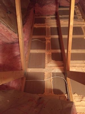Attic with pink insulation between wooden supports and a central pathway of particle board.