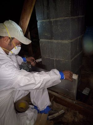 Person in protective suit working on a cinder block chimney in an attic.