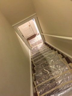 Staircase covered in plastic sheeting, leading to a doorway. Walls are painted a light color.