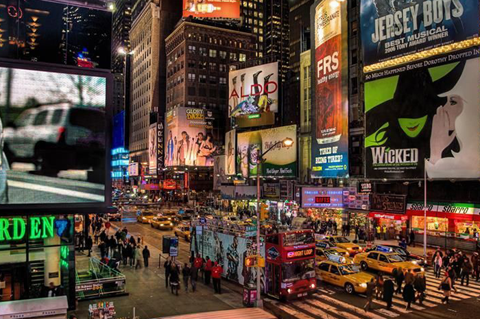 Times Square at night, bustling with people and illuminated billboards, including advertisements for