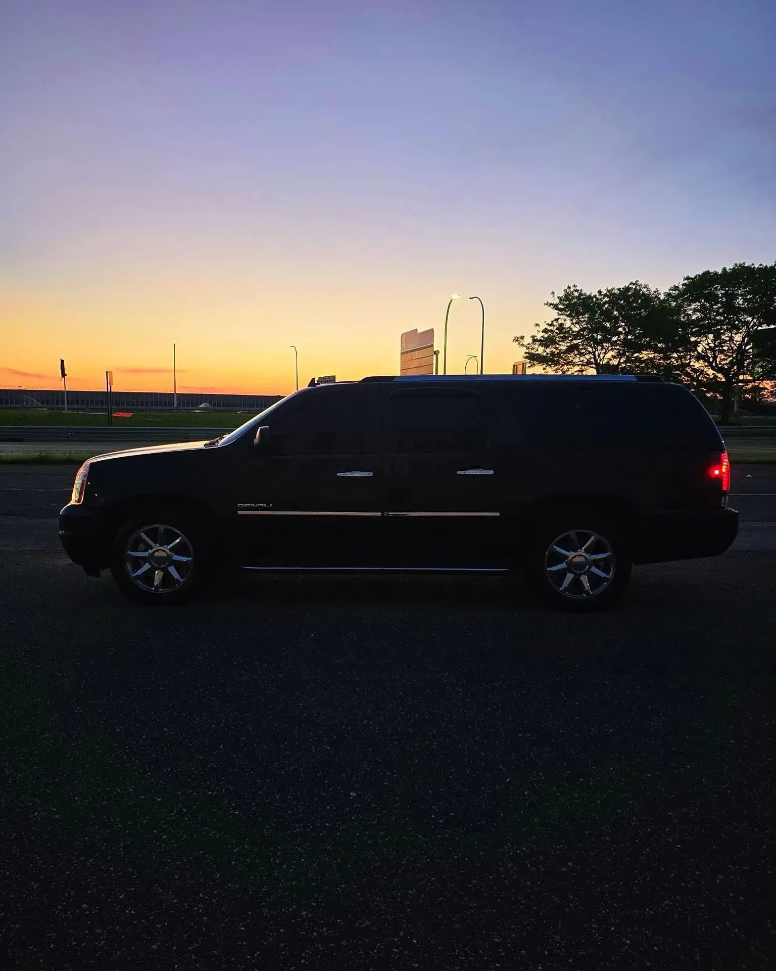A black SUV is parked on the side of the road at sunset.