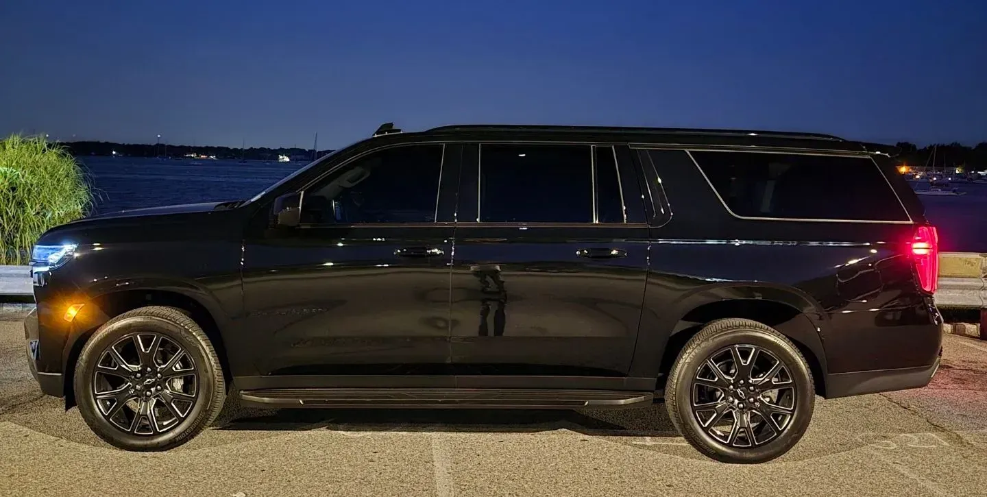A black SUV is parked in a parking lot next to a body of water at night.