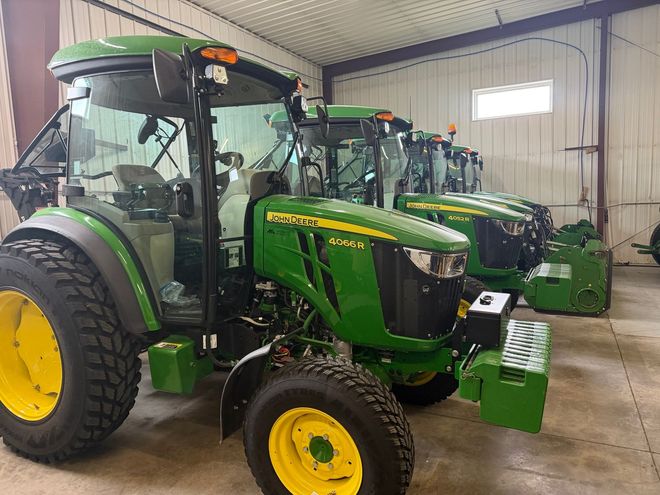 Two green John Deere tractors parked inside a metal workshop
