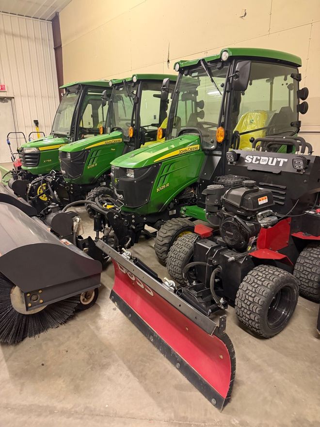 Green lawn tractors and a red snowplow in a garage or workshop