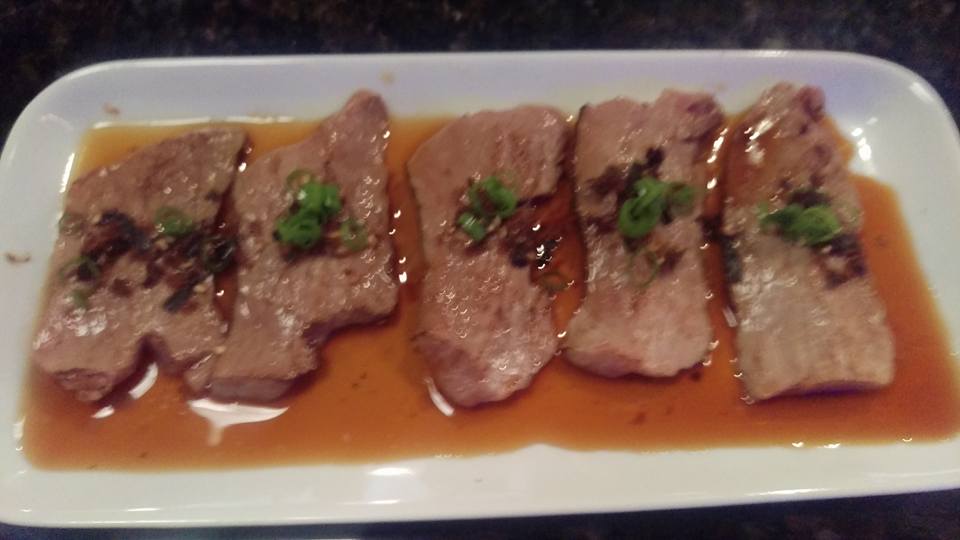 A white plate topped with meat and sauce on a table.