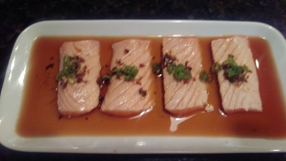 A white plate topped with slices of salmon and sauce