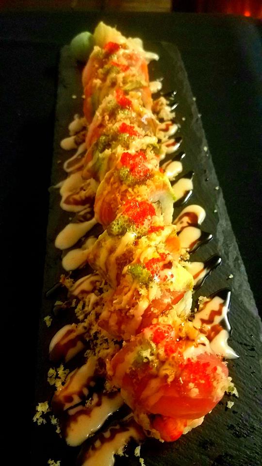 A close up of a sushi roll on a black plate on a table.
