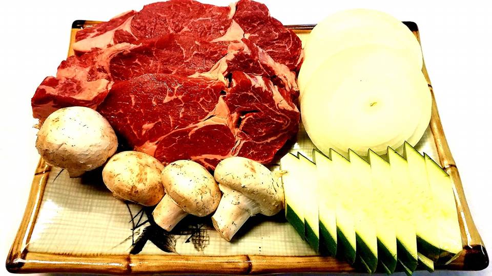 A plate of meat , mushrooms , and onions on a bamboo cutting board.