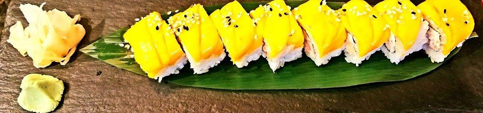 A row of yellow sushi on a green leaf on a table.