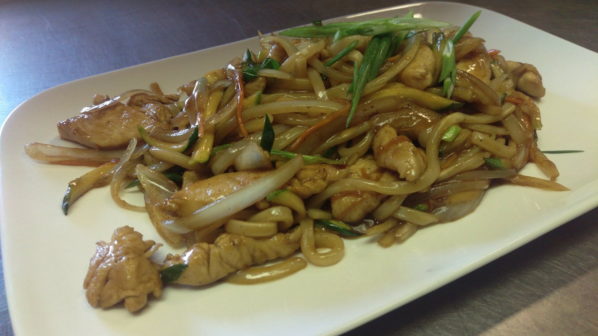 A white plate topped with noodles and meat on a table.