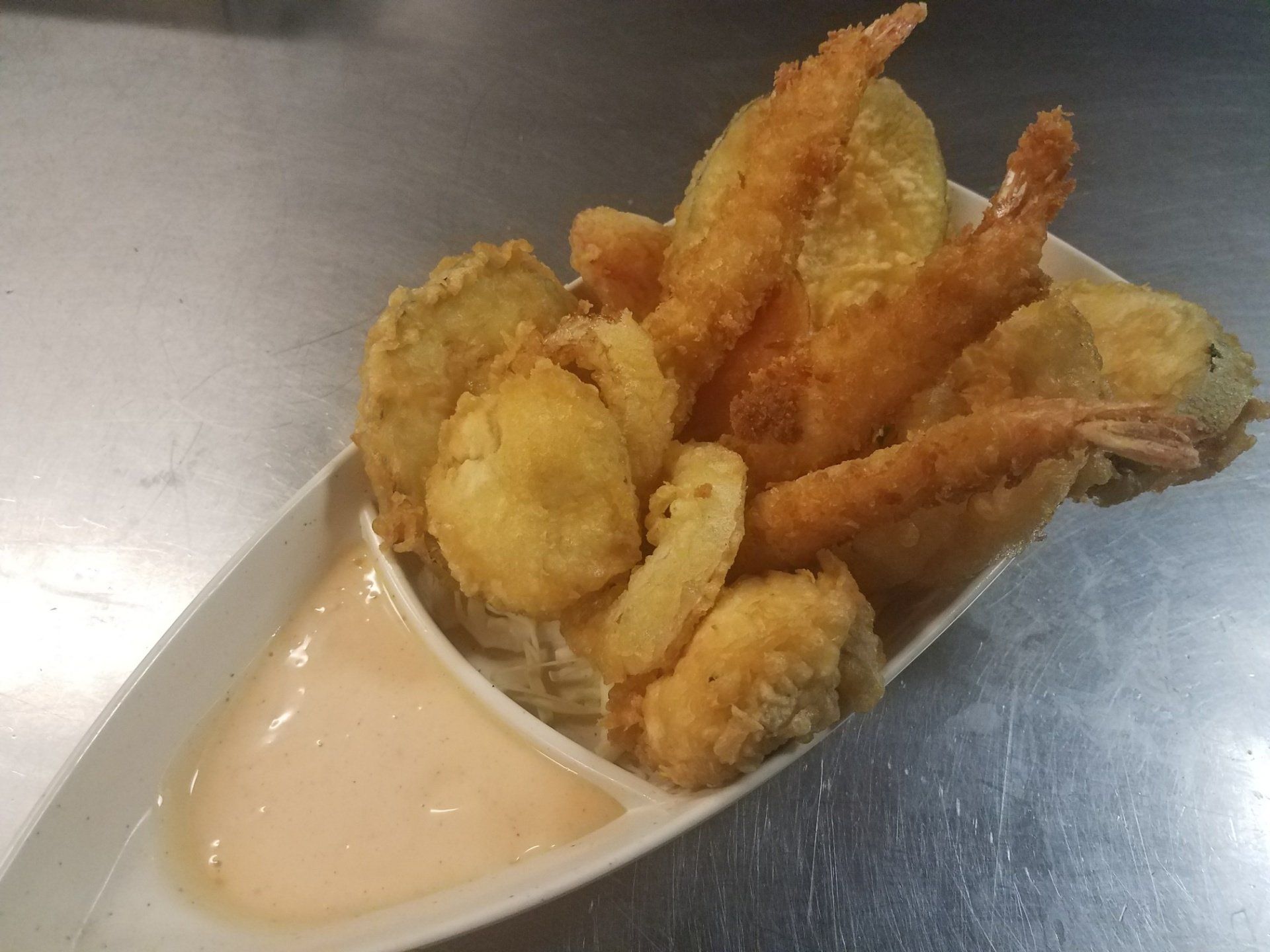 A white bowl filled with fried food and sauce on a table.