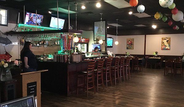 A restaurant with a bar , tables and chairs and balloons hanging from the ceiling.