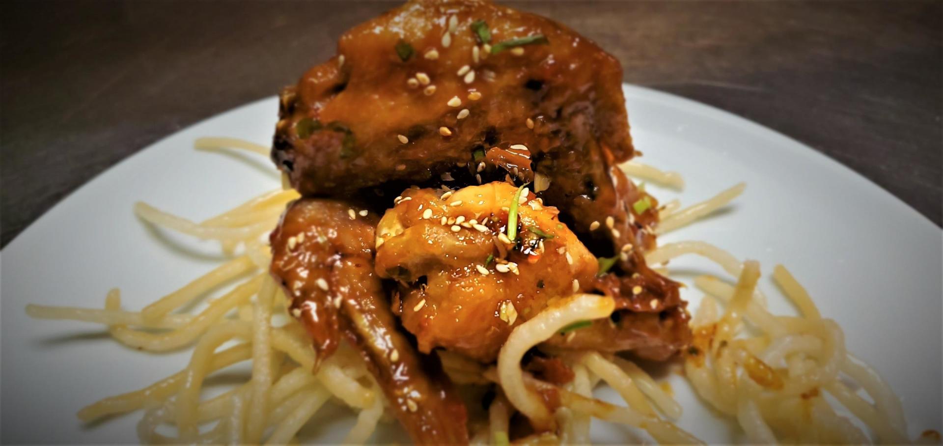 A close up of a plate of food with noodles and meat on a table.