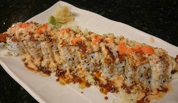 A long piece of sushi on a white plate on a table.