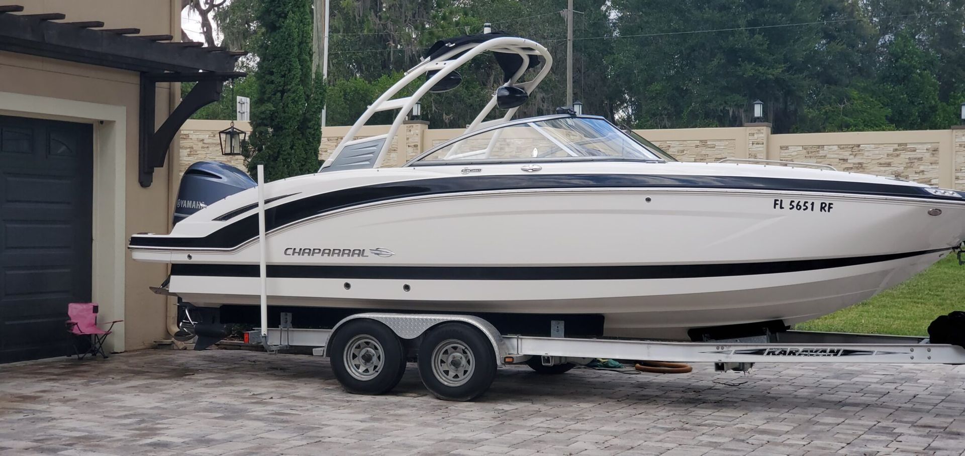 White boat on a trailer parked near a garage, with a black accent stripe.