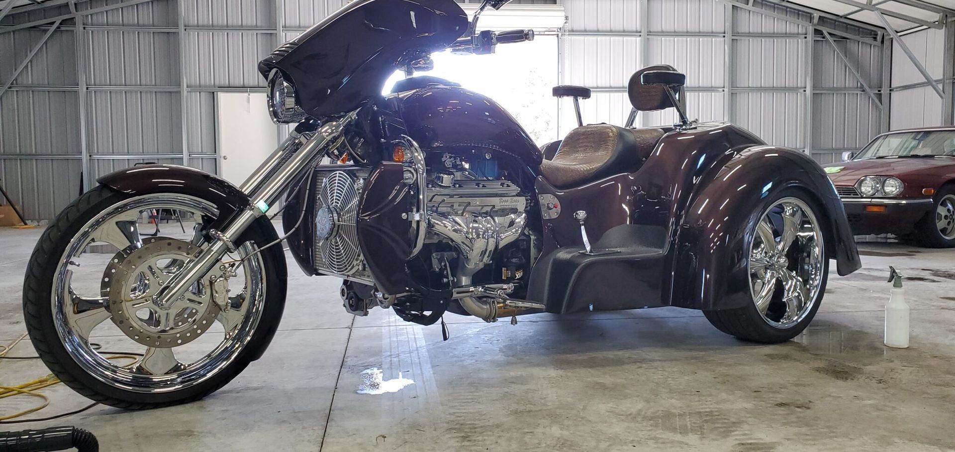 Custom dark burgundy trike motorcycle with chrome wheels, indoors.