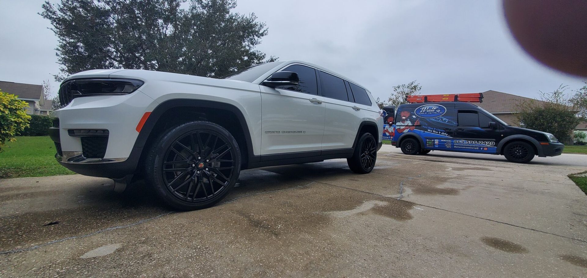 White SUV and black van parked on a driveway, cloudy day.