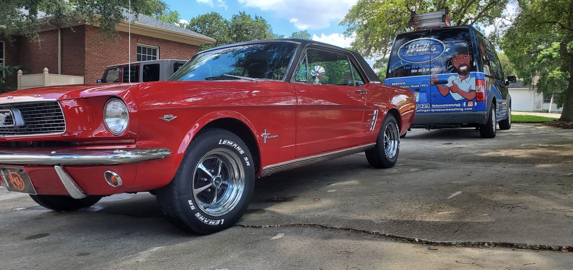 Red classic Mustang car parked next to a blue van with a cartoon on it.