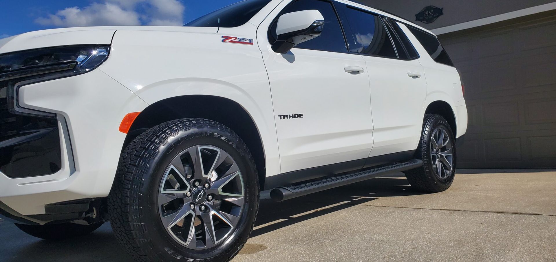 White Chevrolet Tahoe SUV parked on a paved driveway, under a bright blue sky.