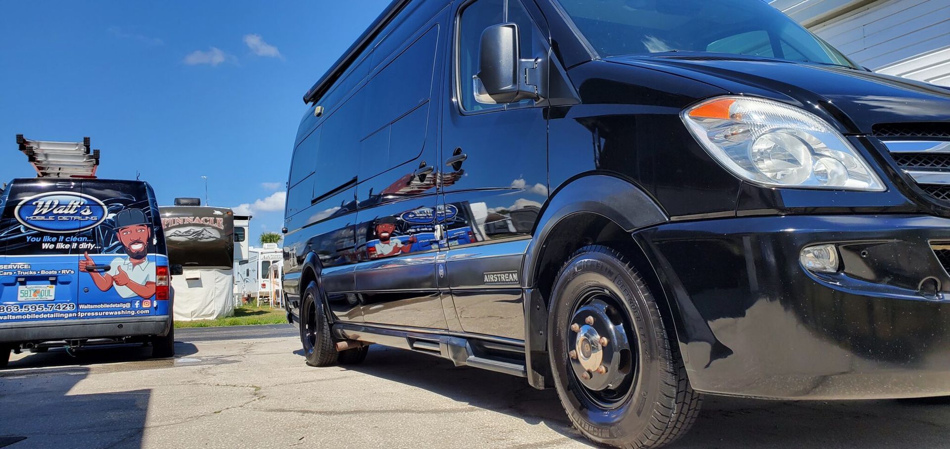 Two black vans parked outdoors under a blue sky. One has a company logo on it.