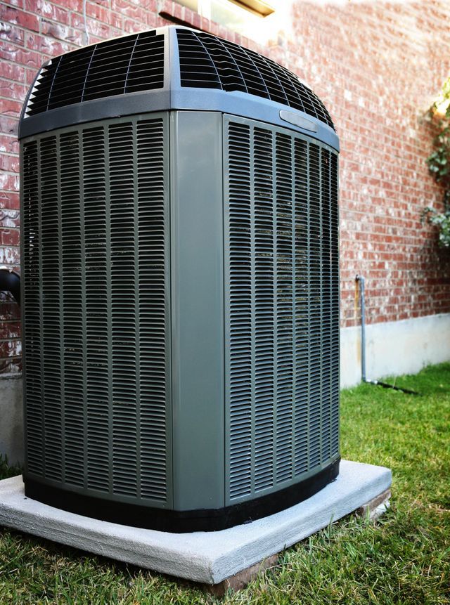 A large air conditioner is sitting in the grass in front of a brick building.