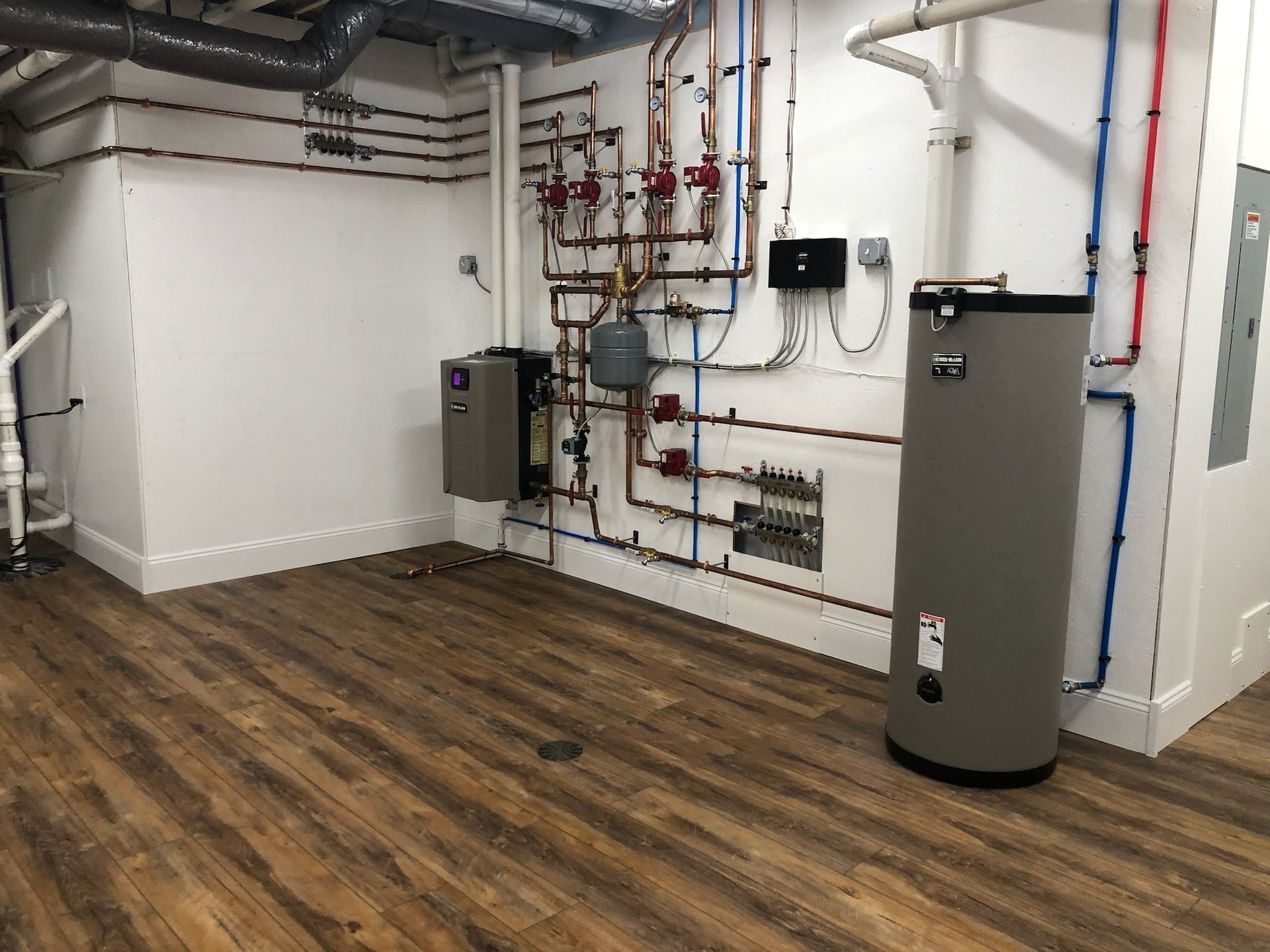 A room with a water heater and pipes on the wall.