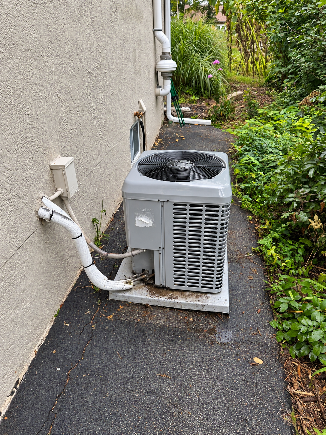 Outdoor air conditioner unit beside a stucco wall along a narrow walkway