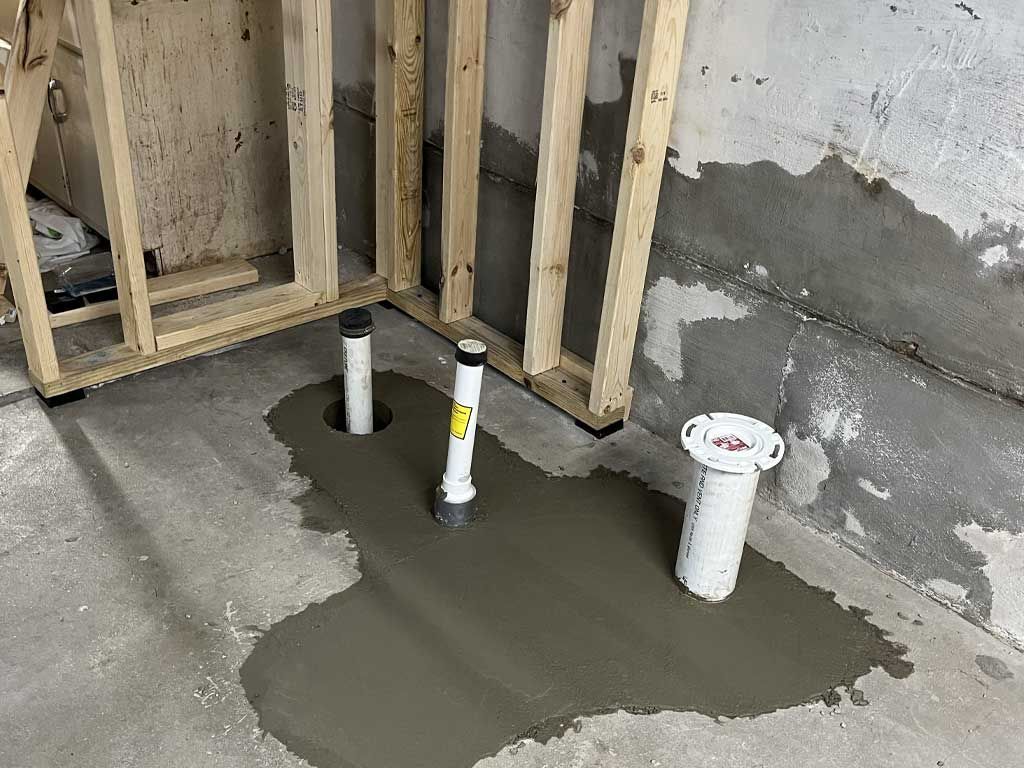 Fresh concrete patch around plumbing pipes in an unfinished wall frame