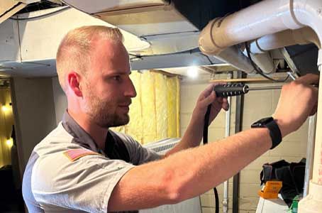 Man tightening a bracket on exposed pipes in a basement utility room