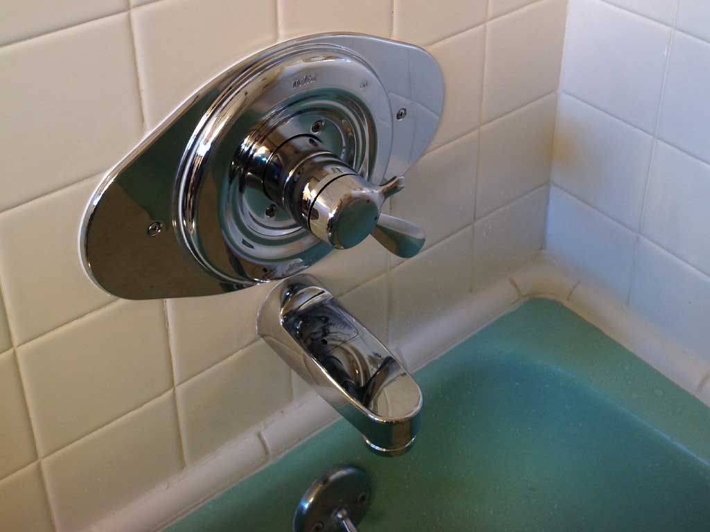 Chrome bathtub faucet and control handle on white tiled wall above a tub